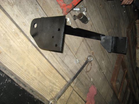 1978 Ford Bronco - A black metal bracket, possibly a vehicle part, lies on a wooden floor next to a wrench and other tools.
