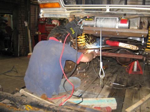 1978 Ford Bronco - A mechanic welds the front frame of a 1978 Ford Bronco in a workshop.