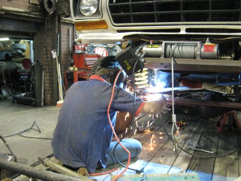 1978 Ford Bronco - A mechanic welds a winch onto the front frame of a 1978 Ford Bronco in a workshop.