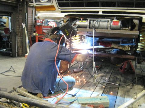 1978 Ford Bronco - Mechanic welding on the frame of a 1978 Ford Bronco, with a winch installed on the front.