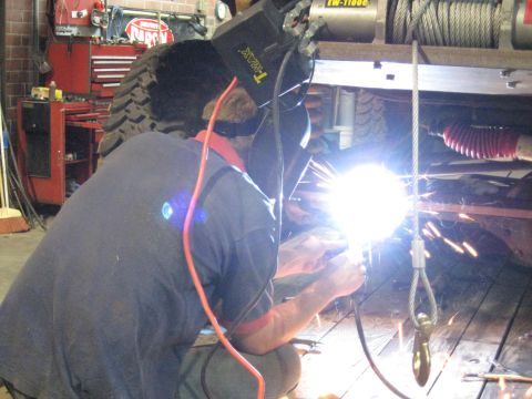 1978 Ford Bronco - A mechanic is welding on the undercarriage of a vehicle in a workshop setting.