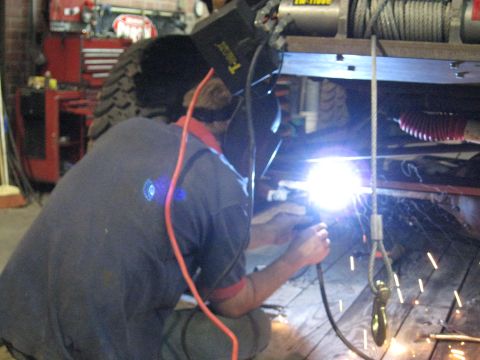 1978 Ford Bronco - A person welds on the underside of a vehicle frame, with a winch visible overhead.