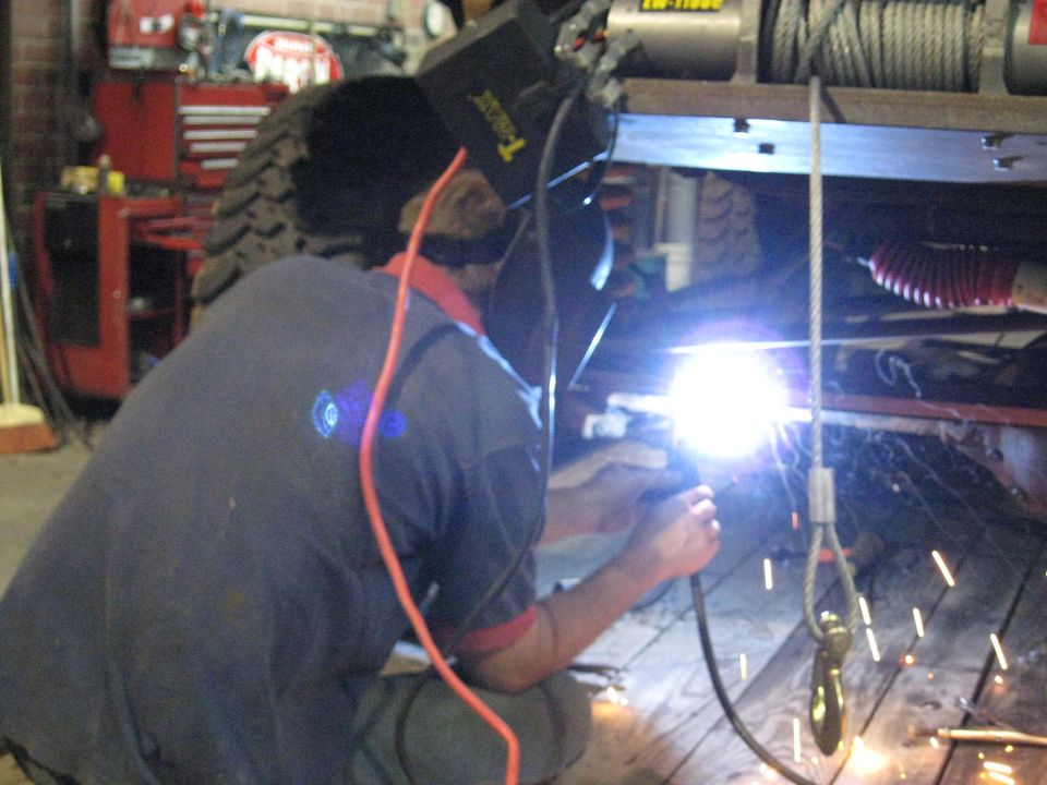 Welder working on vehicle frame with winch above