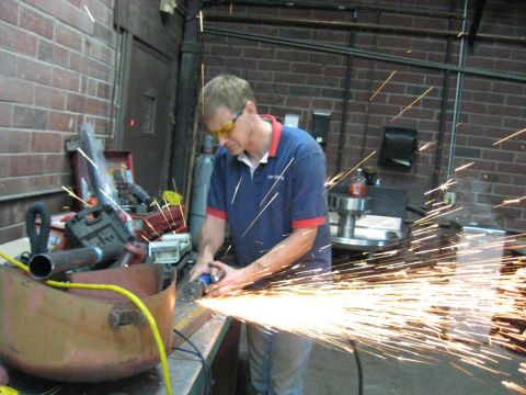 1978 Ford Bronco - A worker uses an angle grinder to cut metal, producing a bright spray of sparks in a workshop.