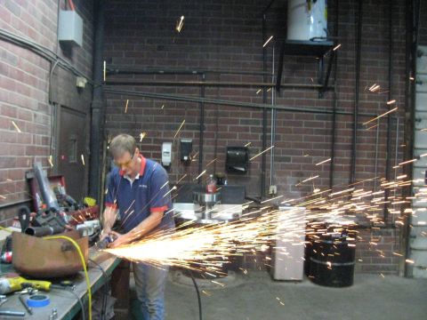 1978 Ford Bronco - A worker uses an angle grinder, generating a bright spray of sparks in a brick-walled industrial setting.