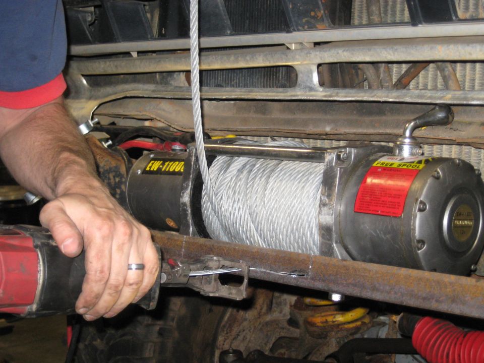 Winch being installed on a vehicle, showing the winch drum, cable, and a person's hands
