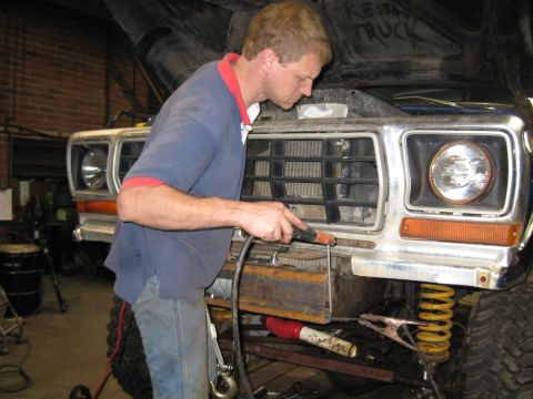 1978 Ford Bronco - A mechanic works on the front end of a truck, welding a custom bumper attachment.