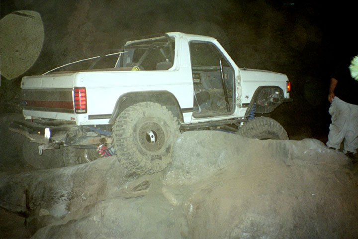 White Ford Bronco SUV crawling over boulders at night with oversized off-road tires