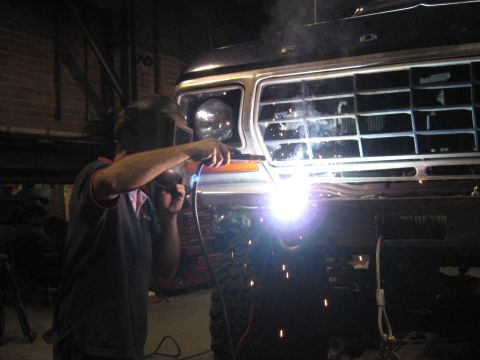 1978 Ford Bronco - A person is welding the front grille of a vehicle, with sparks flying from the torch.