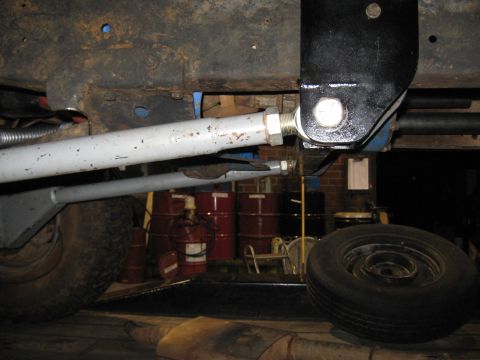 1978 Ford Bronco - Underbody view of suspension linkage and frame, with barrels and a spare tire visible in the background.