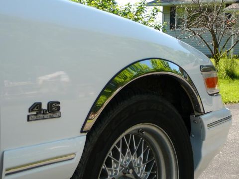 1997 Mercury Grand Marquis - A close-up view of the front fender and wheel of a white sedan, a '4.6 Nitrous Injected' emblem.