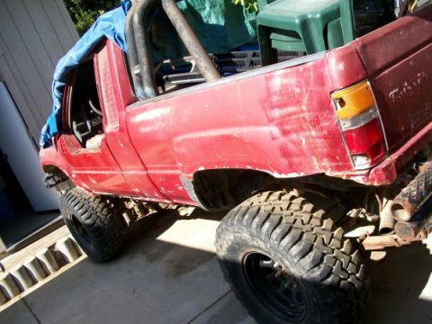 1989 Ford Bronco - Modified red pickup truck with off-road tires and exposed interior.
