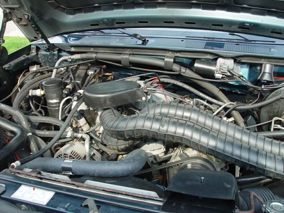 Engine bay of a green vehicle showing air intake, alternator and radiator hose