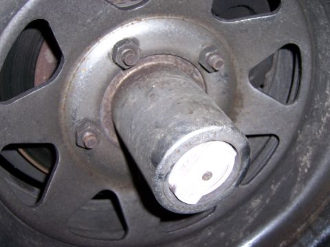 1991 Ford Bronco - A close-up view of a vehicle's wheel hub assembly, showing the lug nuts and a white center cap with visible markings.