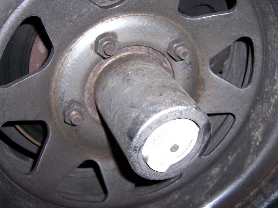 Close-up of a vehicle's wheel hub with lug nuts and a white center cap. Text is visible on the cap
