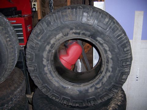 1991 Ford Bronco - A red gas can is placed inside a large off-road tire, which is part of a stack of tires in a garage.
