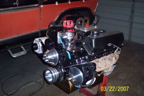 1979 Ford Bronco - A V8 engine is displayed on a stand, partially obscuring the side of a red vehicle.