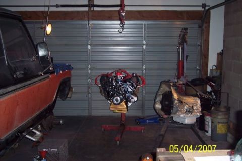 1979 Ford Bronco - An engine and transmission are displayed on stands in a garage, with a vehicle partially visible.