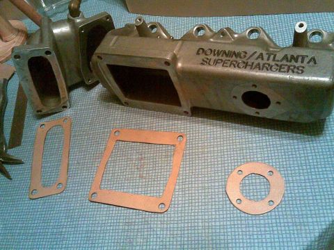 1996 BMW Z3 - Supercharger intake manifold and associated gaskets laid out on a blue checkered surface.