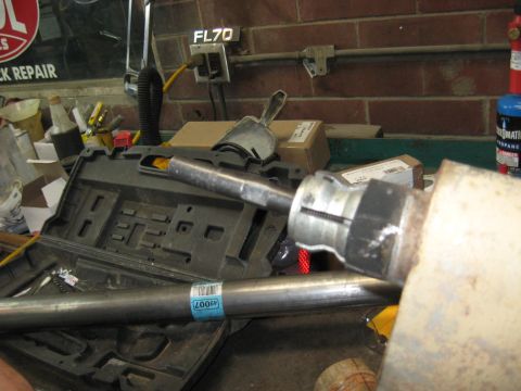 1978 Ford Bronco - Mechanic working on an exhaust pipe, with a tool attached and a part number visible on a label.