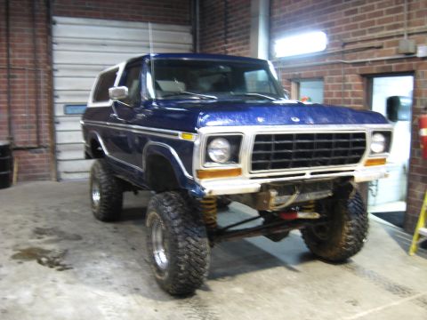 1978 Ford Bronco - A lifted 1978 Ford Bronco in a garage, showing its front 3/4 view and custom suspension.