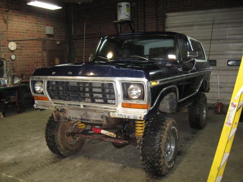 1978 Ford Bronco - A lifted 1978 Ford Bronco sits in a garage, its dark blue paint reflecting the overhead lights.