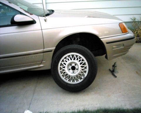 1990 Ford Taurus - Front side view of a 1990 Ford Taurus with a jack on the ground.