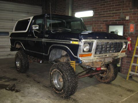 1978 Ford Bronco - A lifted 1978 Ford Bronco with a dark blue body and white top sits in a garage.