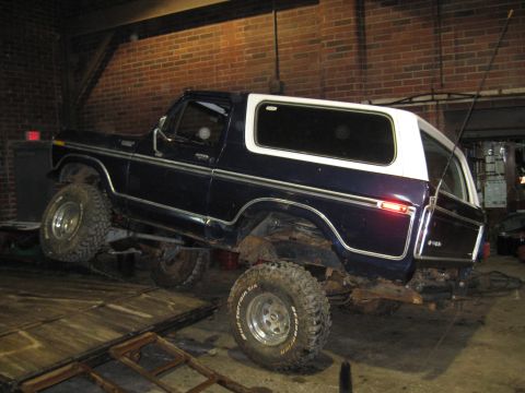 1978 Ford Bronco - Dark blue 1978 Ford Bronco with a white removable top is parked inside a garage.