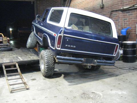 1978 Ford Bronco - A blue 1978 Ford Bronco with a white hardtop is partially loaded onto a trailer in a garage.