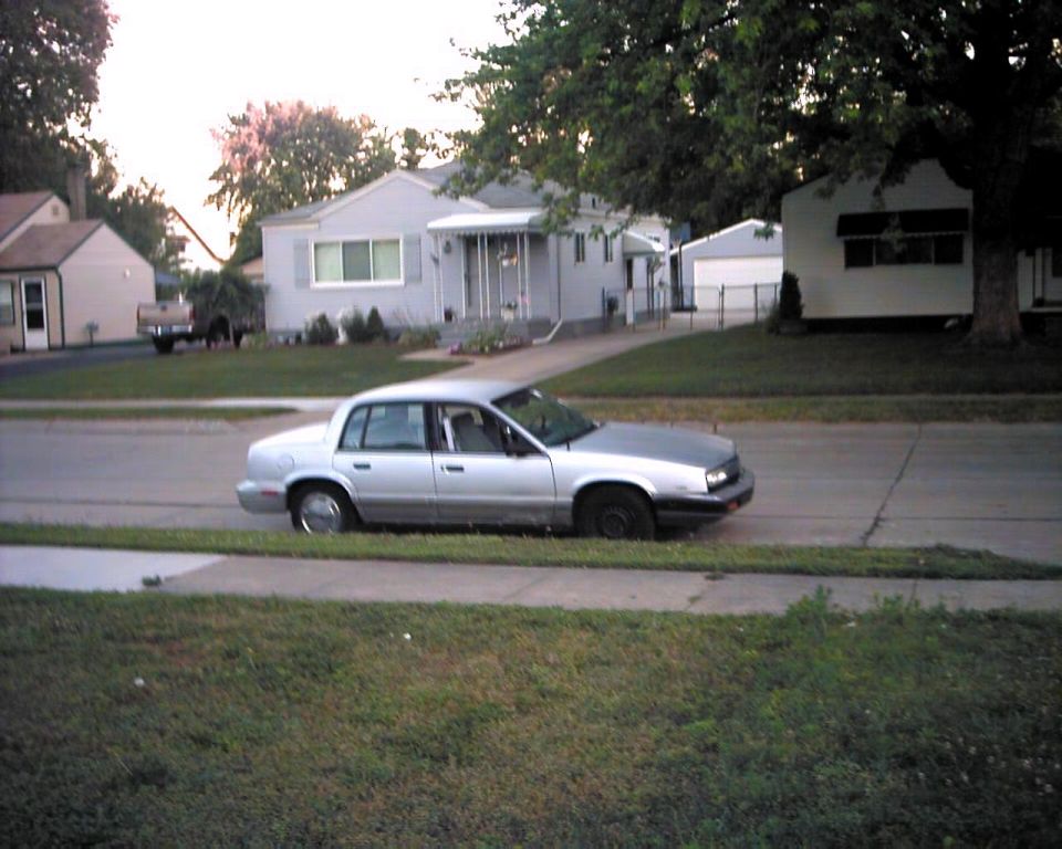 Silver sedan parked on a suburban street, side view. The car has a two-tone paint job with a grey hood