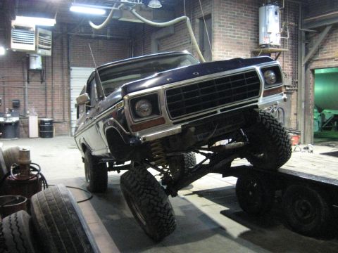 1978 Ford Bronco - A dark blue 1978 Ford Bronco with a lifted suspension is parked on a trailer inside a garage.