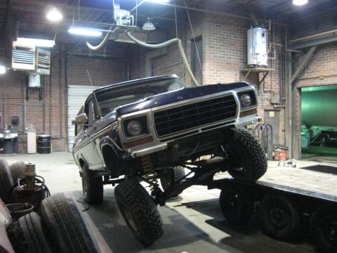 1978 Ford Bronco - A dark blue 1978 Ford Bronco is positioned on a trailer inside a garage, its front-left wheel raised.