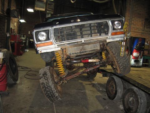 1978 Ford Bronco - Front view of a black 1978 Ford Bronco being worked on, lifted on a trailer in a garage.