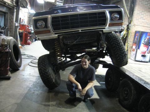 1978 Ford Bronco - A person squats in front of a lifted 1978 Ford Bronco inside a workshop.