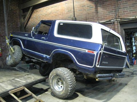 1978 Ford Bronco - A blue and white 1978 Ford Bronco is being lifted onto a trailer in a garage.