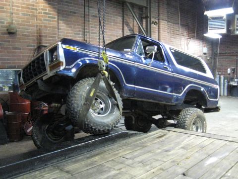 1978 Ford Bronco - A blue 1978 Ford Bronco is suspended by a crane in a workshop, revealing its distinctive body style and front-end details.