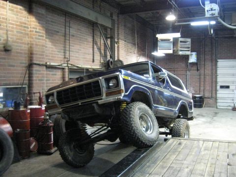 1978 Ford Bronco - A blue Ford Bronco is positioned on a ramp in a workshop, its lifted suspension and large tires.