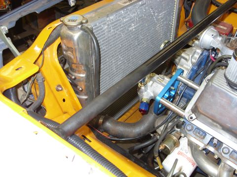 1978 Ford Mustang II - Yellow car engine bay during build showing aluminum radiator, custom overflow tank, and blue AN line fittings.