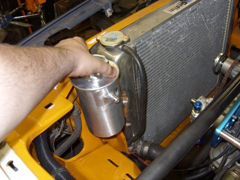 1978 Ford Mustang II - A hand holds an aftermarket aluminum power steering fluid reservoir next to a vehicle's radiator.