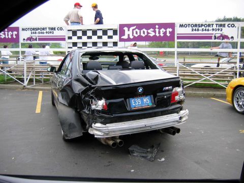 1971 Ford Ranchero - A severely damaged black BMW M5 is parked on a track surface, with a yellow sports car visible to the right.