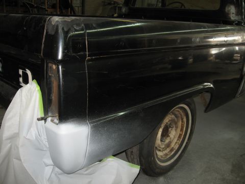 1966 Ford F-100 - The rear quarter panel of a black pickup truck is shown, with primer applied to the lower section of the fender.