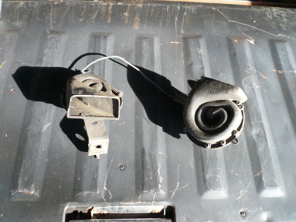 Two car horns, one rectangular and one spiral-shaped, resting on a dark textured surface