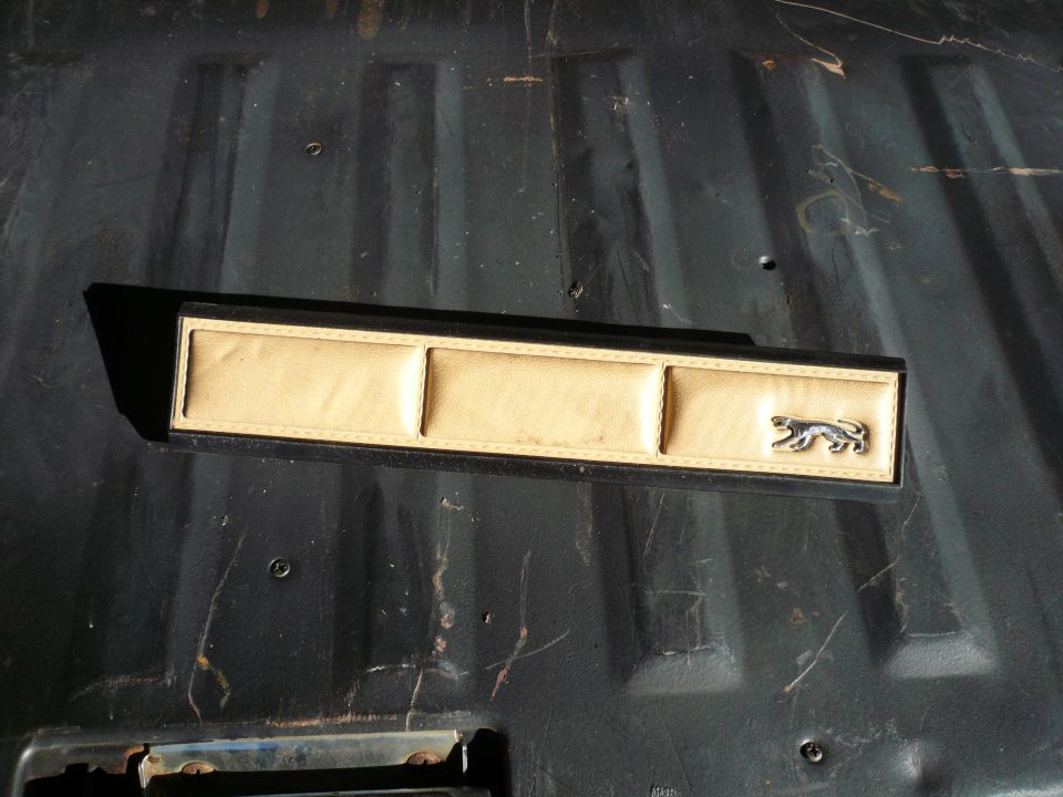 Tan and black interior trim piece with three padded sections and a jaguar emblem
