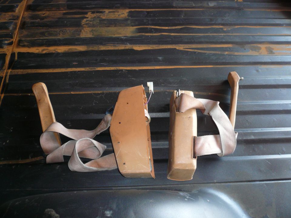 Two tan seatbelt retractors with beige straps on a dark ribbed surface