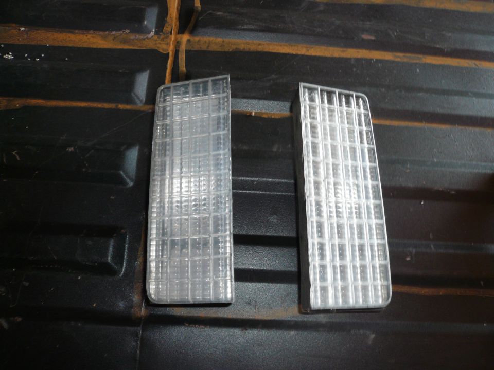 Two clear plastic marker lights with grid patterns, one slightly more worn than the other, resting on a black textured surface