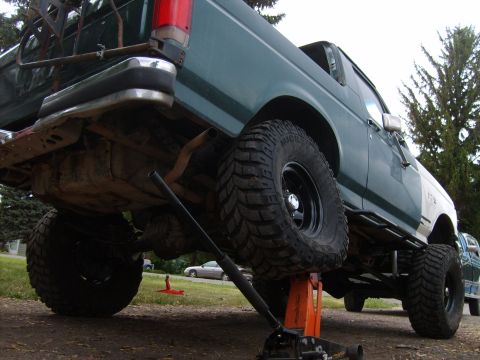 1989 Ford Bronco - A green and white pickup truck is shown lifted on a jack with large off-road tires visible.