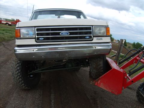 1989 Ford Bronco - A lifted Ford F-Series truck is shown from the front, equipped with a front loader attachment.