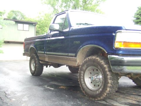1996 Ford Bronco - A blue Ford F-150 pickup truck is parked on a wet driveway in front of a house.