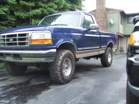 1996 Ford Bronco - A blue pickup truck is parked on a driveway, with another vehicle partially visible in the foreground.